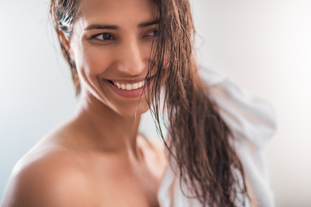 Portrait of satisfied female with brilliant smile keeping hair with towelの写真素材