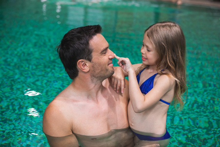 My daddy. Profile of happy father holding daughter in pool. Small girl is looking at man and touching his nose with smile. They are delighted to spend time side by sideの写真素材