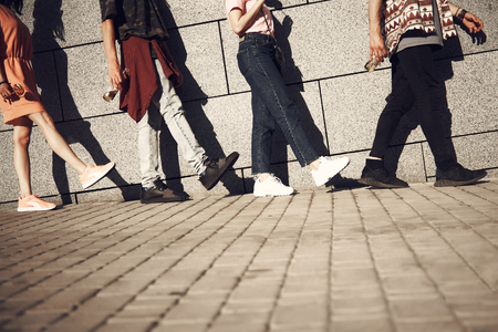 Close up females and men feet moving one after another. Guys keeping bottles with beverage in hands. Copy spaceの写真素材