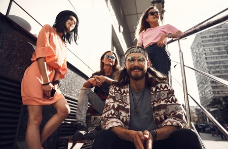 Low angle outgoing bearded male in modern glasses situating near thoughtful girls and pensive guy. Wistful lady holding phone in handsの写真素材