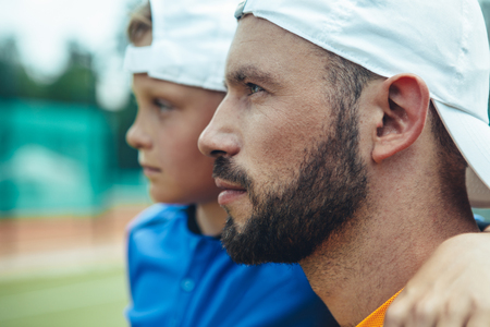 Side view orderly little boy embracing serene young unshaven sportsman outdoorの写真素材