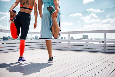 Sporty couple is standing on top of high urban building above city. They are standing on one foot...