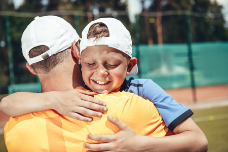 Happy boy with closed eyes embracing father while locating on court. Glad relationship conceptの写真素材