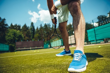 Close up male legs in modern sneakers situating on green ground. He training with racket in armの写真素材