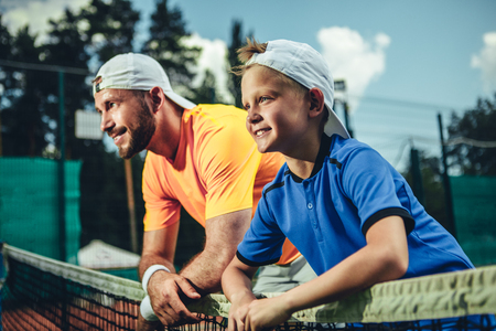 Side view positive boy and beaming bearded male relaxing after good tennis playの写真素材