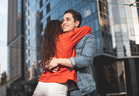 Side view of happy man meeting girlfriend in city with smile. She is turning back and hugging boyfriend with joyの写真素材