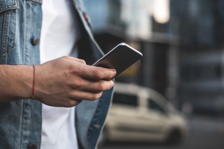 Close up focus on male hand holding mobile outdoors. Young guy is communicating online and typing on screen. Copy space in right sideの写真素材