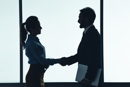 Side view outgoing female greeting with satisfied male employer during communication. They keeping gadgets in armsの写真素材