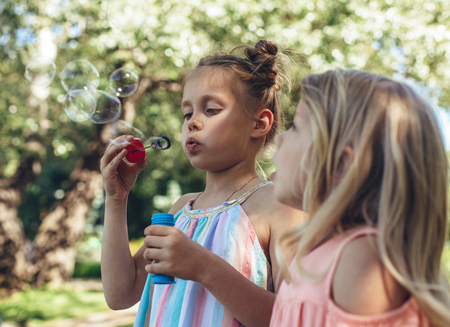 Side view of little girl standing and blowing soap bubbles. Her sister is looking beside with amazementの写真素材