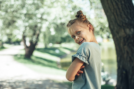 Side view of delighted small girl standing outdoors with folded hands. She is looking at camera with joy. Copy space in left sideの写真素材