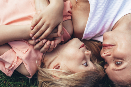 Top view of caring mother resting on grass with little kid. They are looking at each other with contentの写真素材