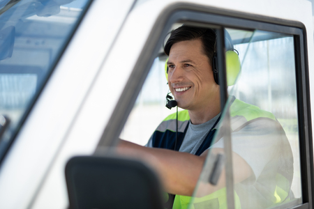 Happy driver. Side view of cheerful airport worker driving the car. He is wearing headphones with microphoneの写真素材