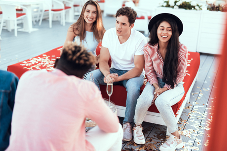 Positive male communicating with beaming ladies while sitting on cozy sofa outdoorの写真素材