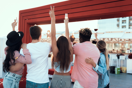 Young ladies and males gesticulating hands while drinking alcohol beverage. They turning back to cameraの写真素材