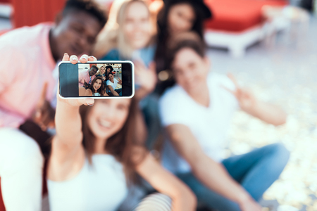 Close up girl hand holding phone. Cheerful friends doing photo on itの写真素材