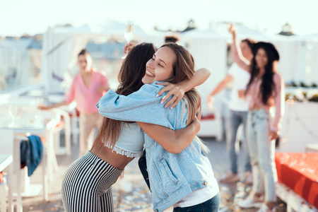 Outgoing lady hugging best friend while holding glass of beverage. Meeting of glad comrades conceptの写真素材