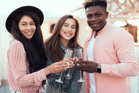 Portrait of beaming ladies and satisfied male tasting alcohol liquid while looking at camera during celebrationの写真素材