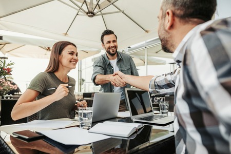 Good job. Cheerful friends making a deal at cafe. Beautiful happy woman sitting at the table with laptops and holding pen