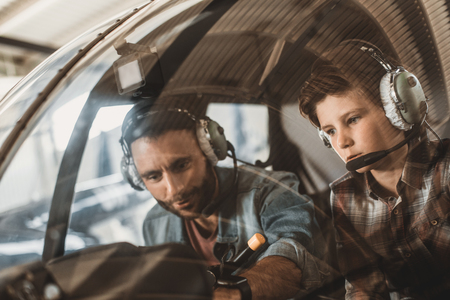 Portrait of concentrated boy and smiling unshaven father adjusting control while wearing headsets....