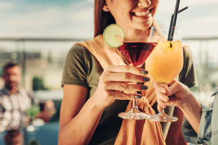 Taste good. Close up of women hands with alcohol drinks. Lady standing at rooftop cafe and smilingの写真素材
