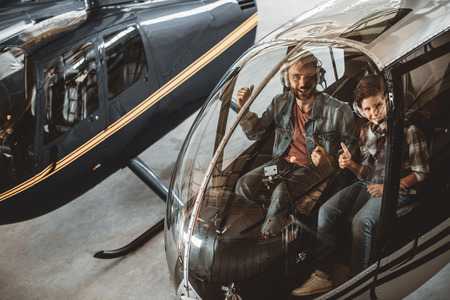 Portrait of smiling unshaven man and happy guy expressing cool while looking at camera. They sitting in cabin of helicopterの写真素材