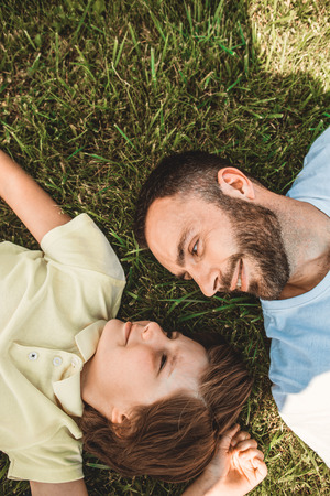 Side view laughing bearded father telling with positive male child during relax. Glad dad and son having leisure together conceptの写真素材