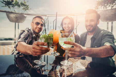 Having fun. Smiling men and lady celebrating on the rooftop cafe. Focus on alcohol drinksの写真素材