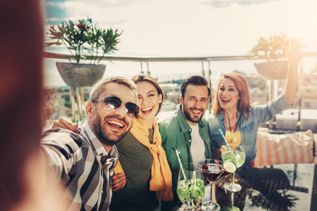 Beautiful shot. Group of young smiling people taking photo. Various cocktails standing on the tableの写真素材