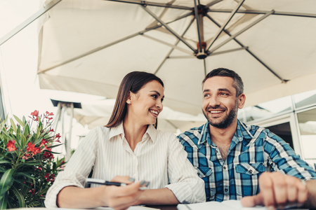 Happy together. Beautiful lady holding pen and looking at cheerful bearded manの写真素材