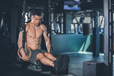 Strong sportsman is doing L sit with gymnastic outfit. He is balancing in support position and...