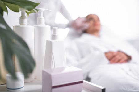 Good skincare. Close up of beauty tools on the table at cosmetologist cabinet. Woman in soft bathrobe getting injection on backgroundの写真素材