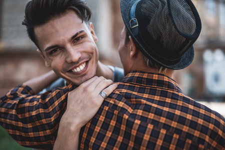 Pleased guy embracing man while looking at camera. They locating in city outsideの写真素材