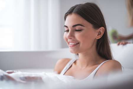 Portrait of beaming girl taking bath while entertaining. She looking at her hands in foamの写真素材
