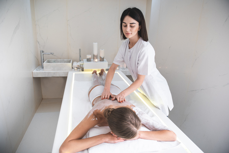 Good day at spa. Beautiful lady lying on massage table and having spa procedure with white clayの写真素材