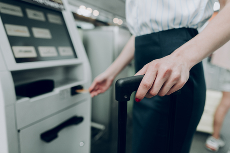 Close up of female hand is holding suitcase, while inserting bank card into cash dispenserの写真素材