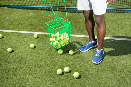 Man is standing on court and keeping basket with balls. He is preparing for playing match on sunny playground. Exercising during sport competition conceptの写真素材