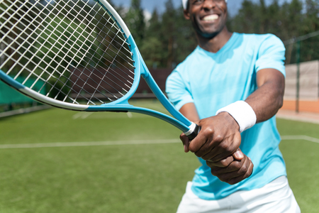 Close up of racket while merry guy is holding it with both hands. Athlete is ready for striking ball with equipment. Playing sport with joy conceptの写真素材