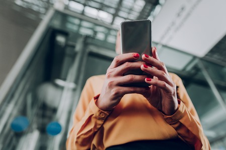 Active use. Low angle portrait of girl holding cellphone with both handsの写真素材