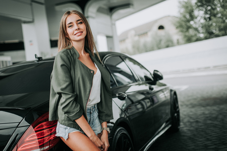 Portrait of outgoing sexy young lady situating near contemporary car outdoor. She expressing happiness. Glad female during journey conceptの写真素材