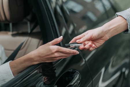 Close up female arm giving key from modern car for girl. She locating in vehicle while putting arm...