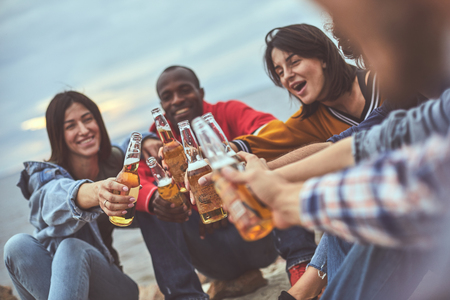 Portrait of friendly team drinking alcohol during their vocation. Focus on clinking of glass bottlesの写真素材