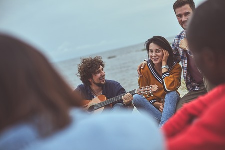 Singing and listening. Group of happy people sitting in circle while smile man jamming on the guitarの写真素材
