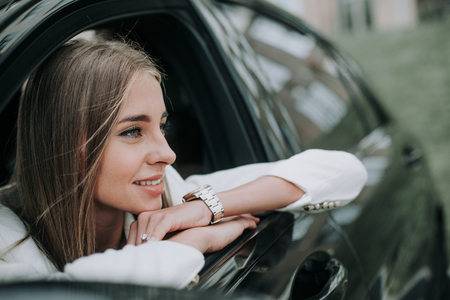 Side view happy woman with attractive smile looking away while locating in modern car. Glad lady thinking during rest in vehicle conceptの写真素材