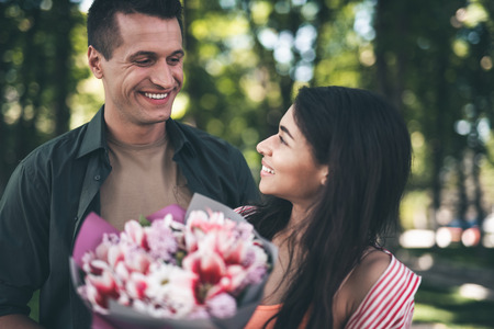 Thankful woman. Cheerful thankful young woman kindly smiling to her positive beloved man after receiving a bouquet of flowers from himの写真素材