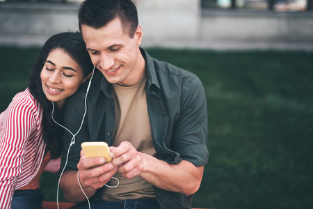 Listening to music. Happy long haired woman smiling and closing her eyes while listening to music in earphones together with her cheerful boyfriendの写真素材