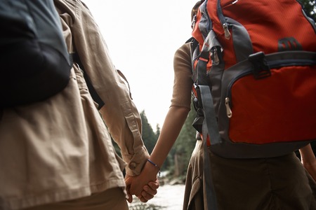 Close view of two travelers carrying heavy backpacks and holding hands while traveling