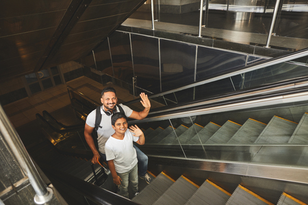 Top view of a joyful hindu man and his nice son standing on the escalator while starting their journeyの写真素材