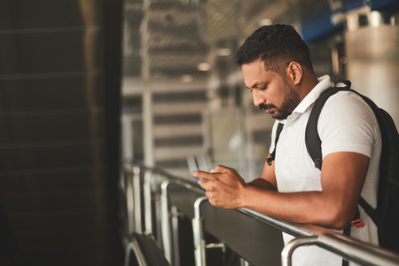 Pleasant serious Hindu man using his phone while standing at the railway stationの写真素材