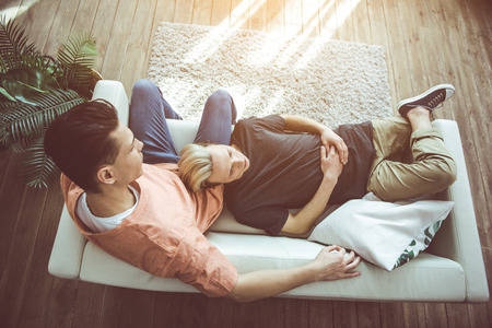 Top view portrait of guy with dyed hair lying on sofa while his boyfriend sitting and looking at himの写真素材