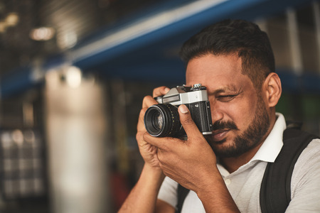 Close up of a delighted Hindu man holding his professional camera while making photos with enthusiasmの写真素材